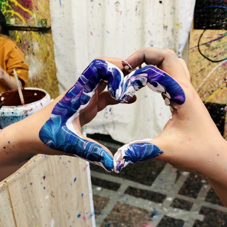 Kinderhände, die zu einem Herz geformt sind, mit bunter Farbe.