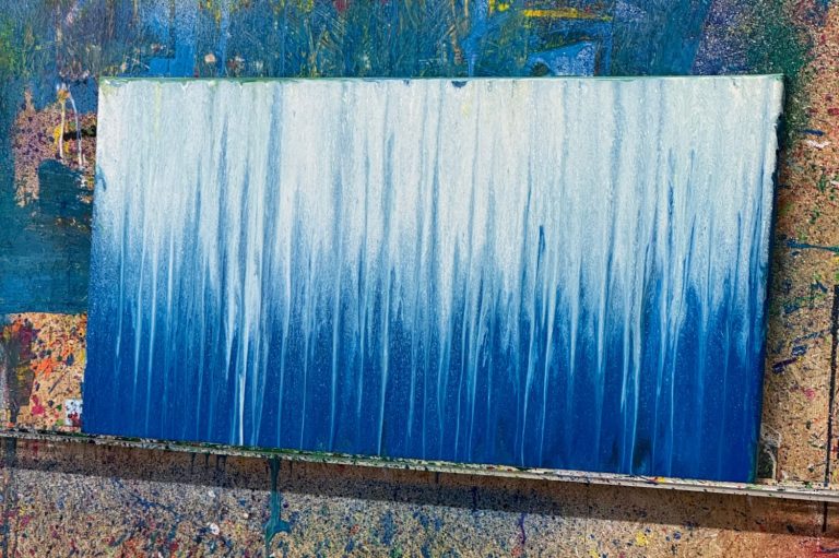 Ein Action-Painting-Bild. Die Leinwand ist mit blauer und weißer Farbe gestaltet, die ineinanderfließt.