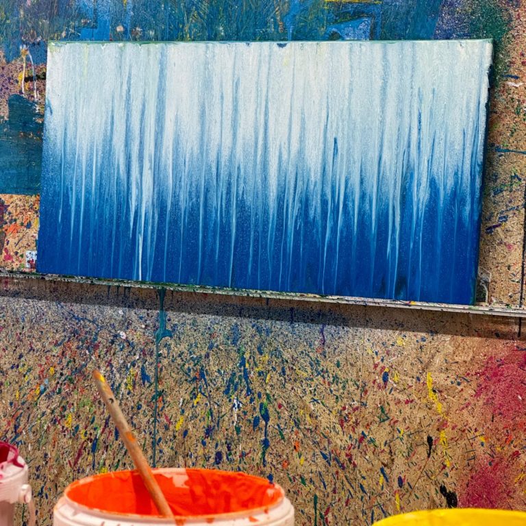 Ein Action-Painting-Bild. Die Leinwand ist mit blauer und weißer Farbe gestaltet, die ineinanderfließt.