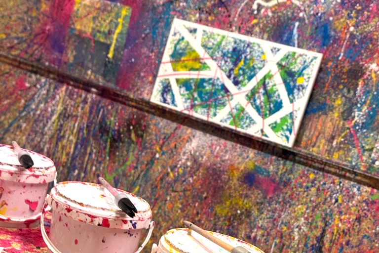 Ein Action-Painting-Raum mit Farbeimern, Pinseln und Farbspritzern.
